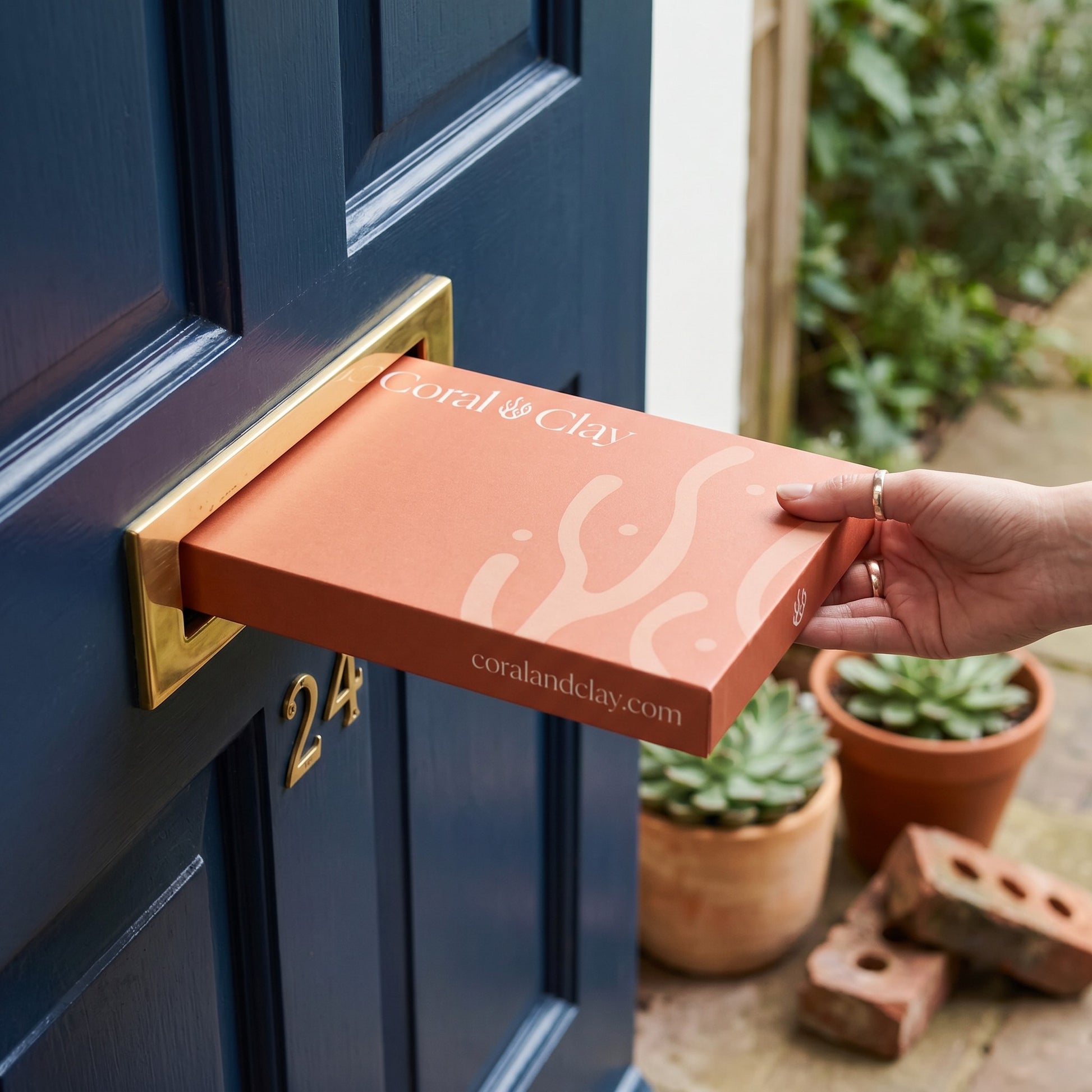 Person posting a Coral & Clay Letterbox Gift through a front door.