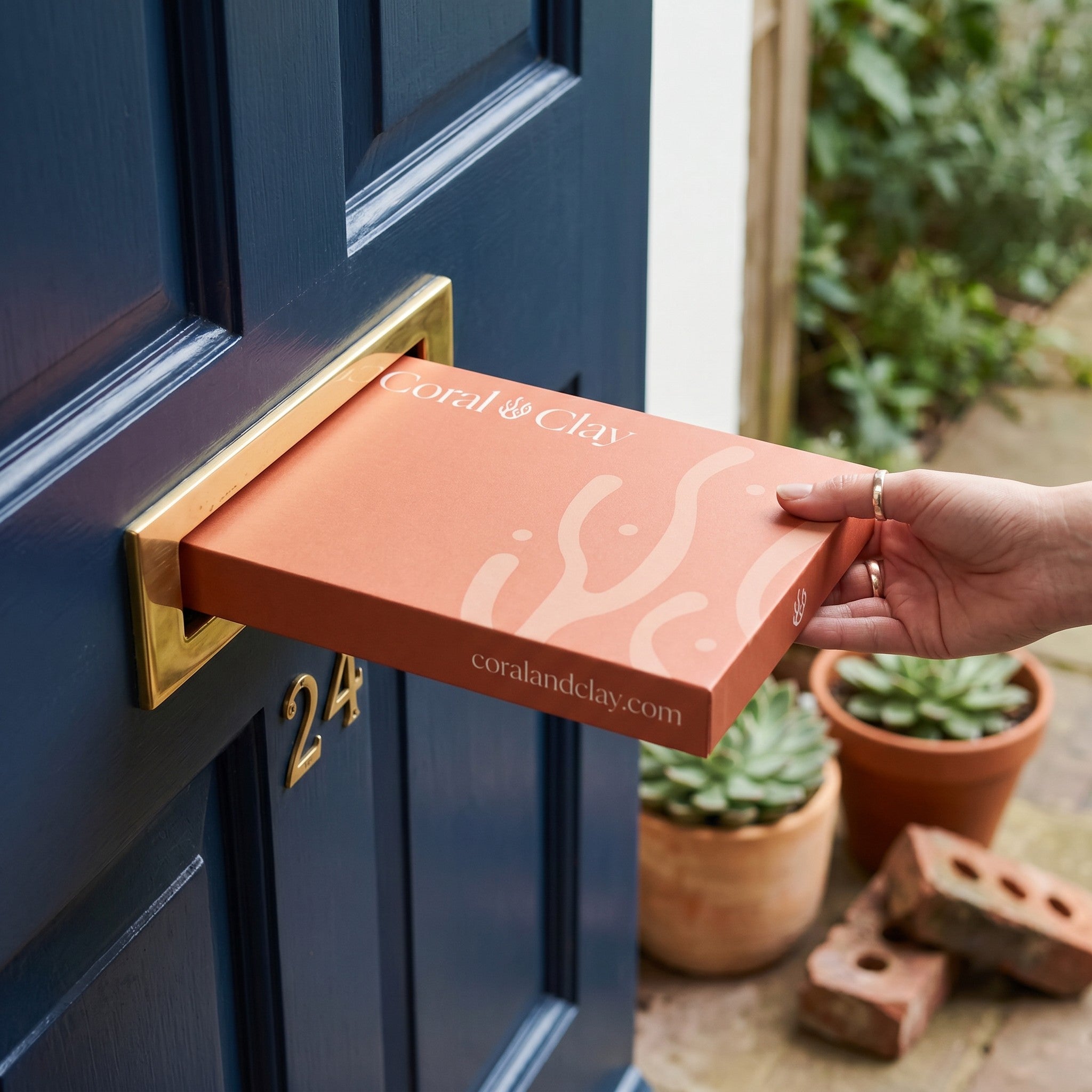 Person posting a Coral & Clay Letterbox Gift through a front door.