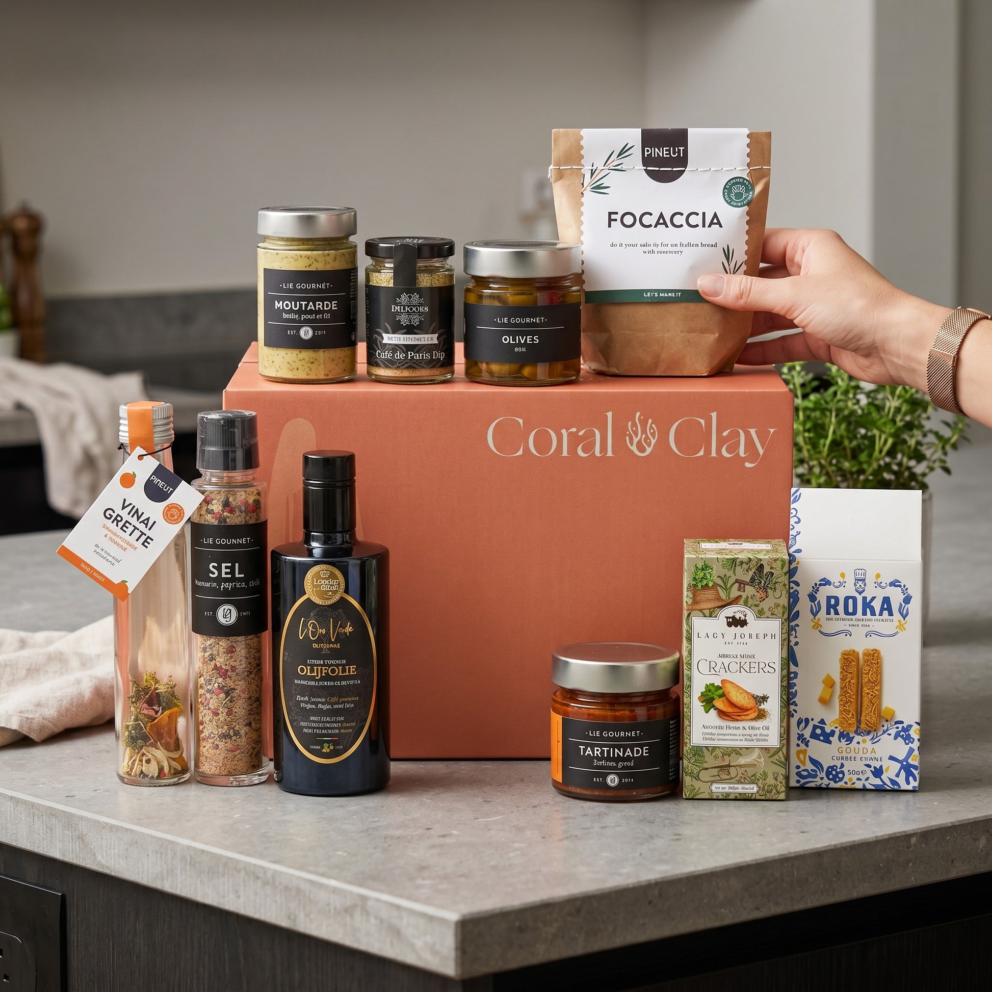 Collection of gourmet food items including jars, bottles, and a Grand Coral & Clay gift box on a kitchen counter.