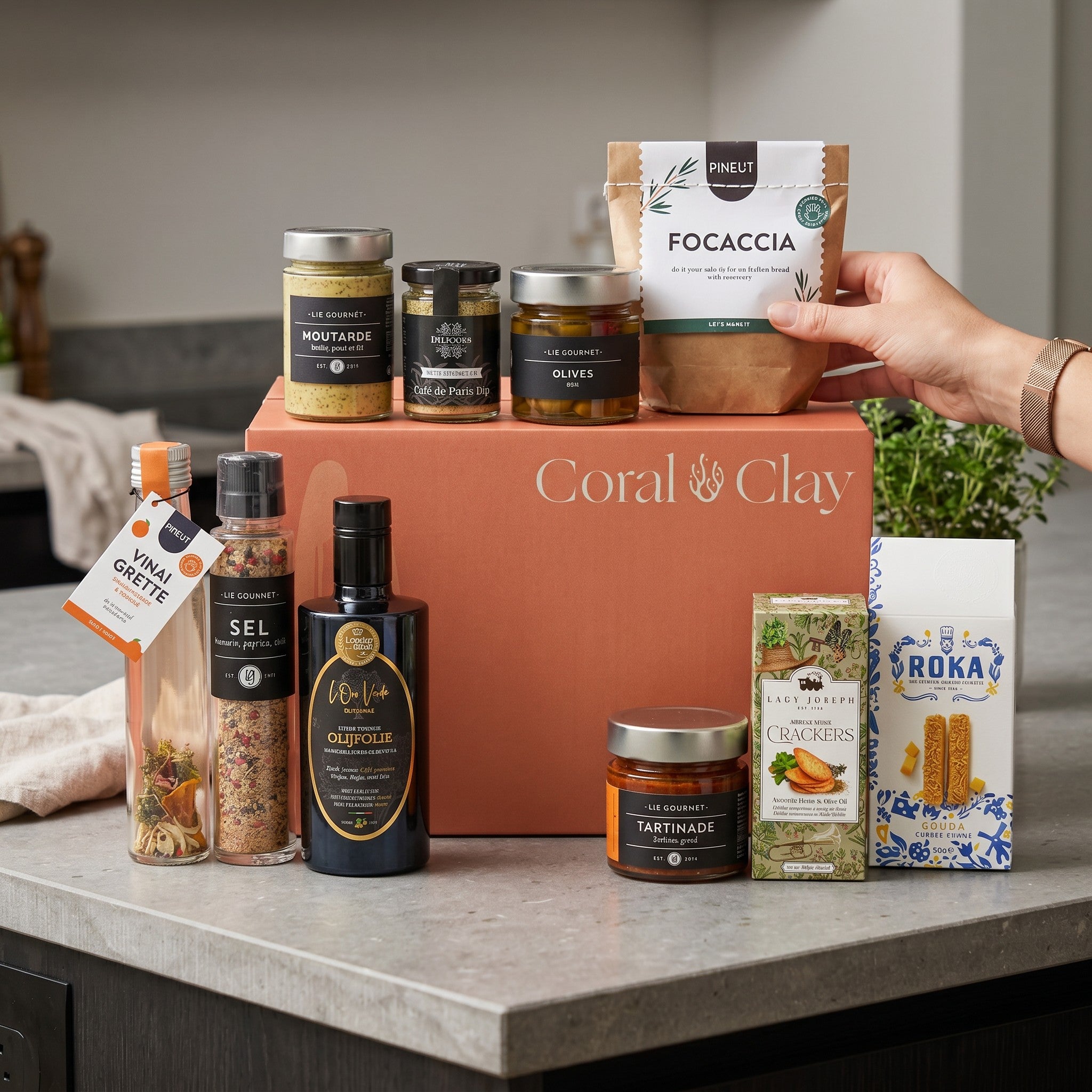 Collection of gourmet food items including jars, bottles, and a Grand Coral & Clay gift box on a kitchen counter.