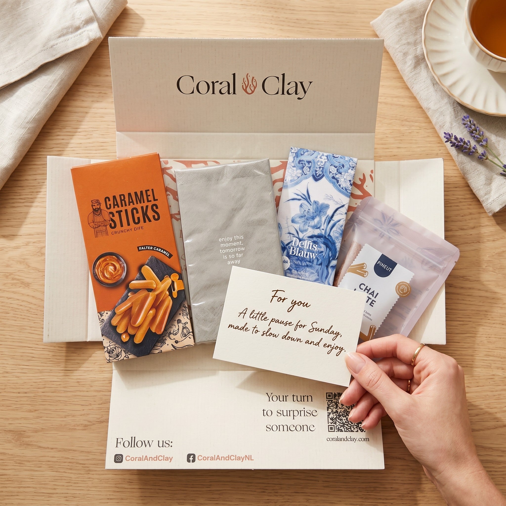 Coral & Clay Sunday Afternoon letterbox gift packaging photo – hand holding a gift card above the chai & chocolate letterbox box on a wooden surface