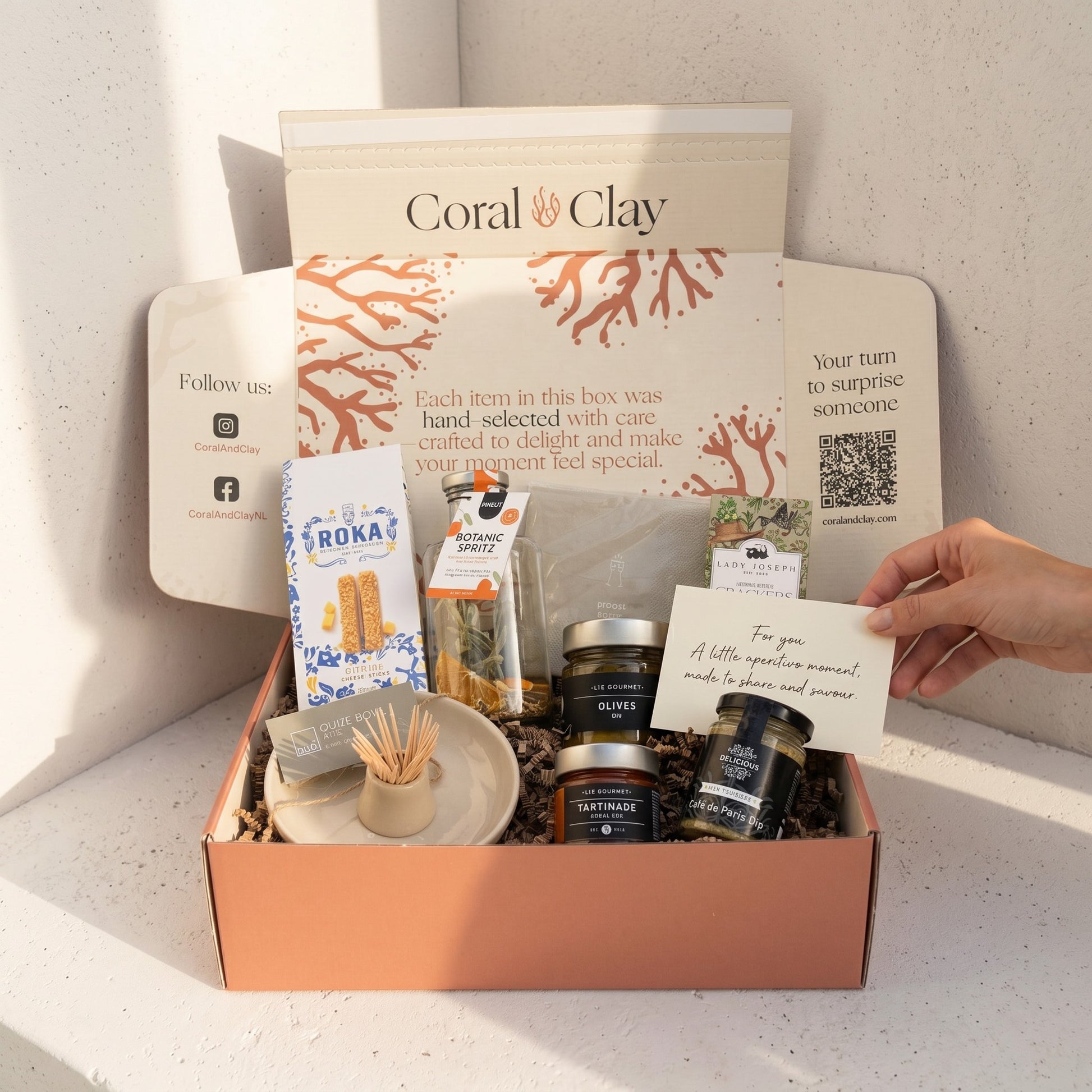 Gift box with various items including a card, branded box, and small containers on a light surface.