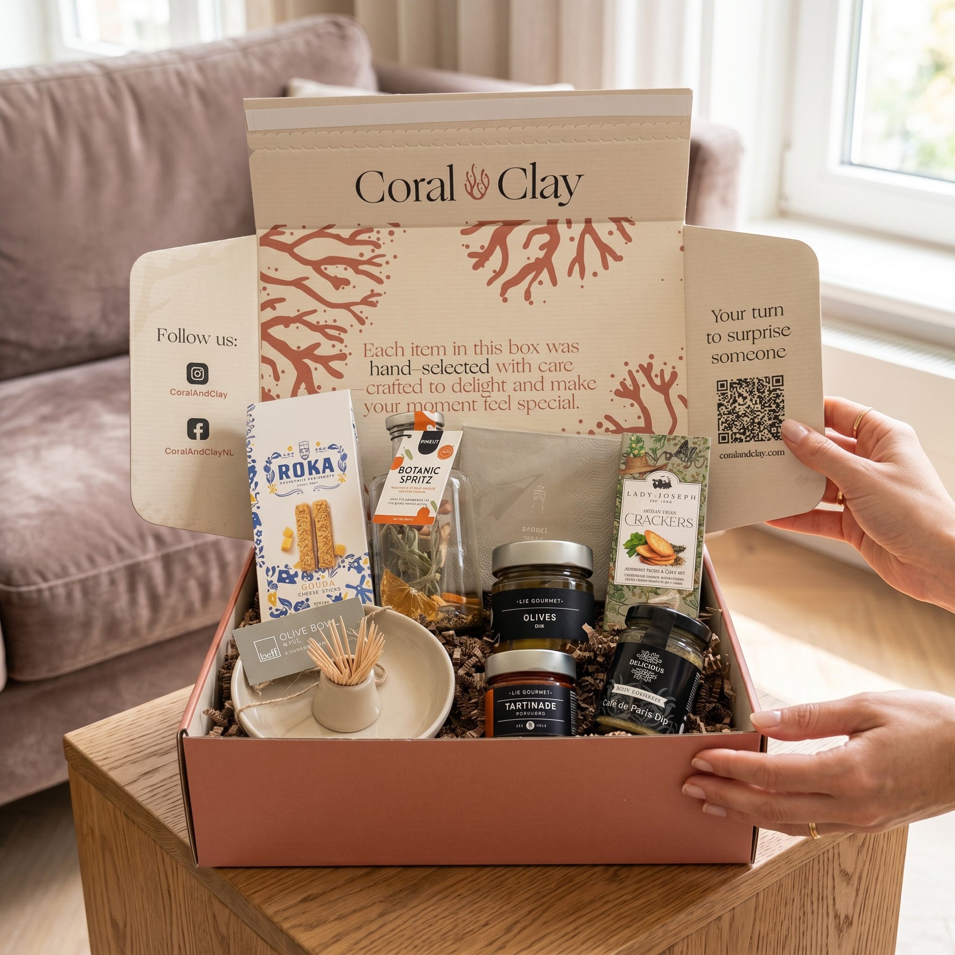 Aperitivo Moments Signature Gift staged shot on wooden table with mocktail mix, chili olives, red pepper tapenade, dip mix, herb crackers, Gouda cheese sticks, olive bowl and napkins.