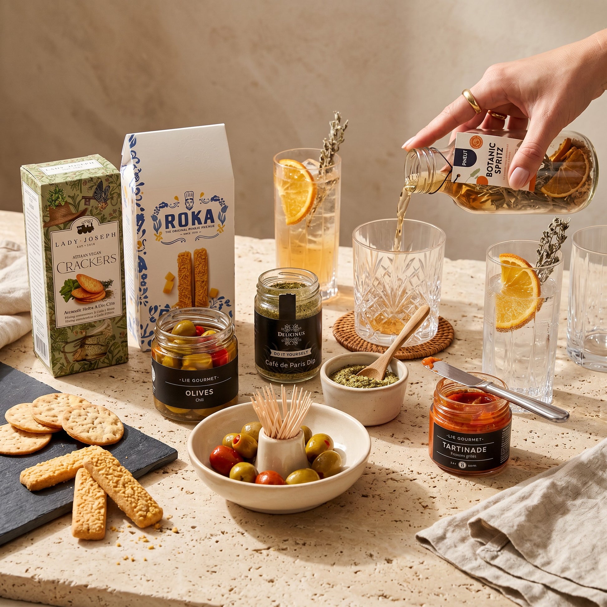 Aperitivo Moments Signature Gift table setting with mocktail, olives, red pepper tapenade, dip mix, herb crackers, Gouda cheese sticks, olive bowl and napkins.