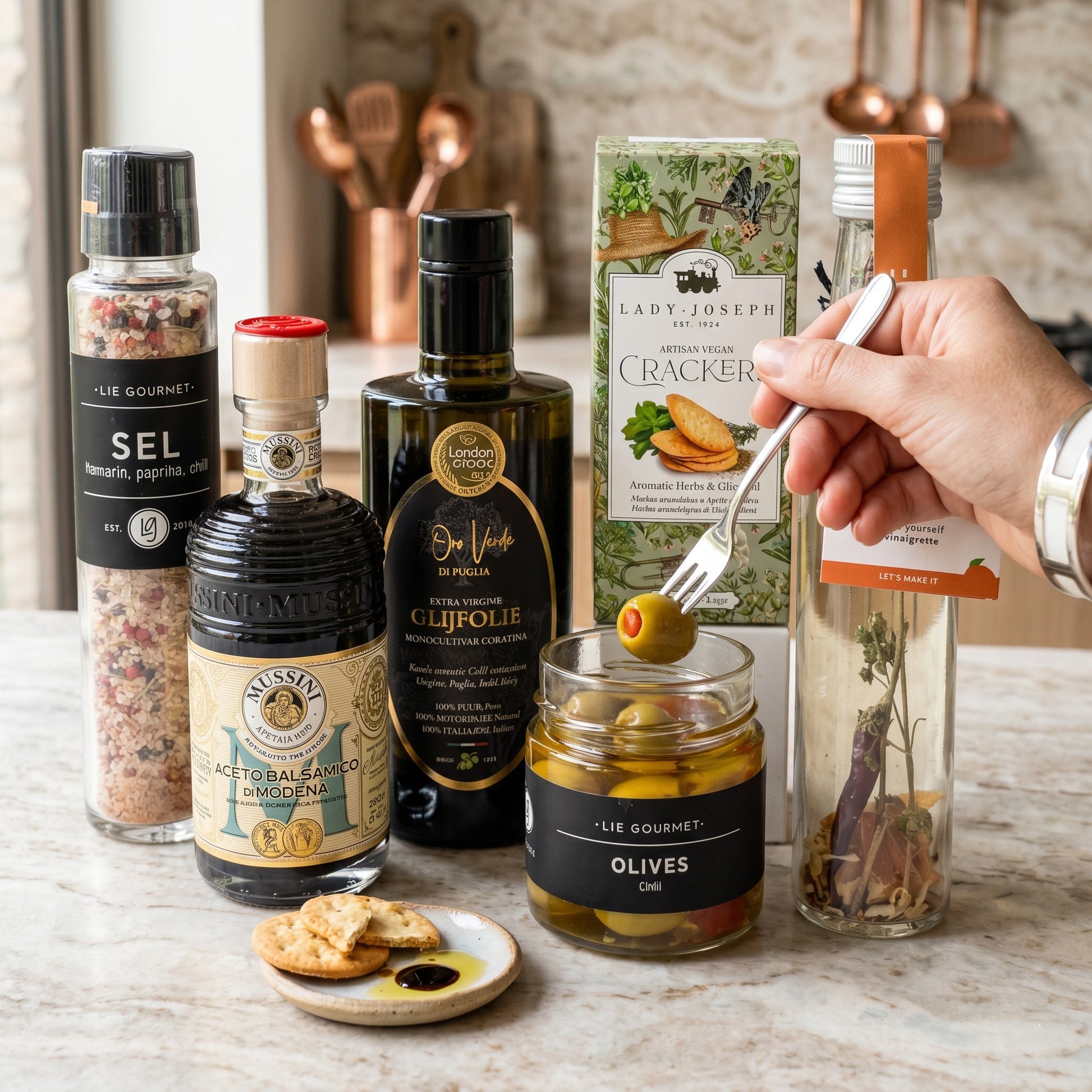 Luxury Mediterranean Signature Gift products on a kitchen counter: olive oil, balsamic vinegar, olives, crackers, vinaigrette and seasoning.