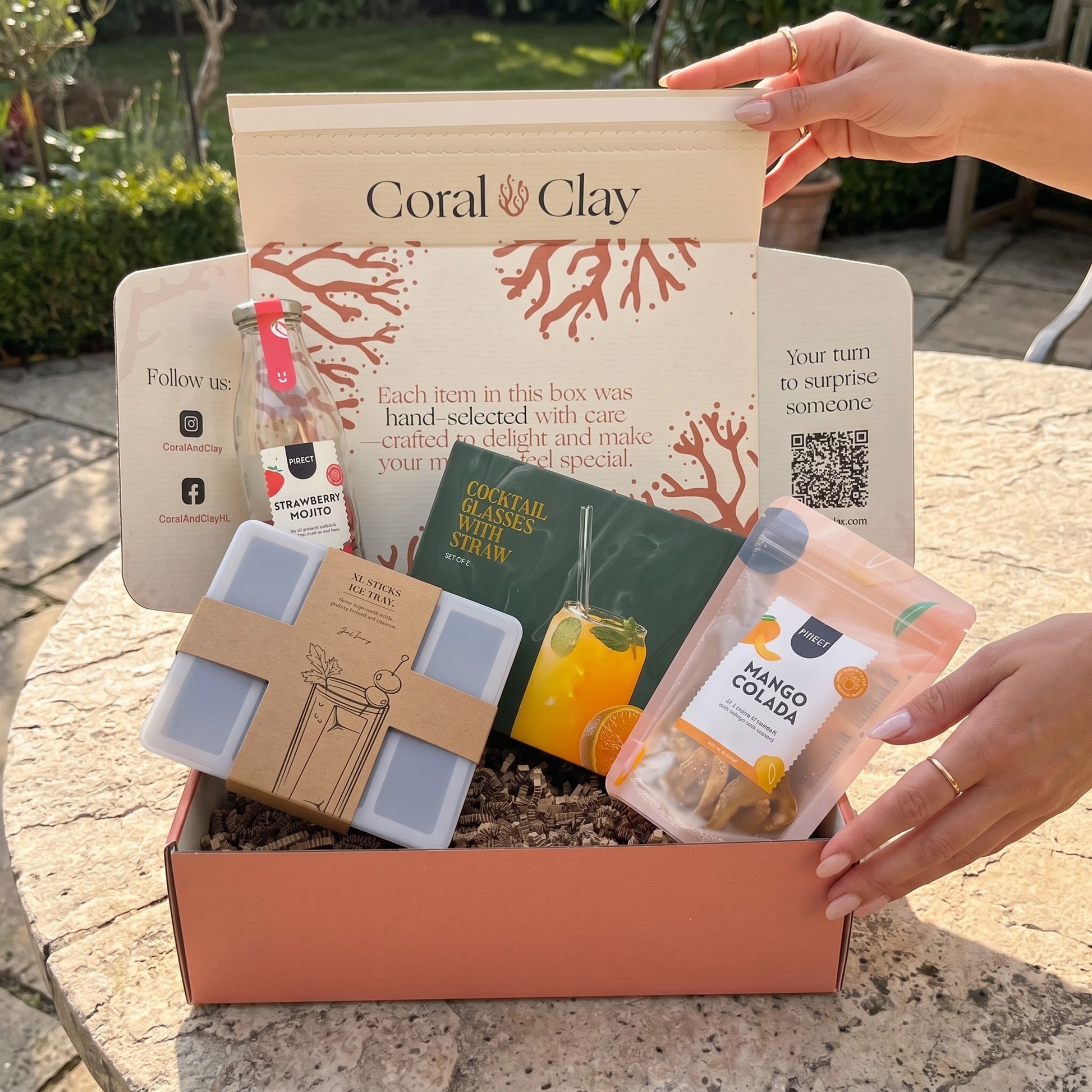 Summer Cocktail Signature Gift outdoor shot on stone surface with strawberry mojito cocktail bottle, mango colada pouch, cocktail glasses with straws, ice cube tray and signature gift box.