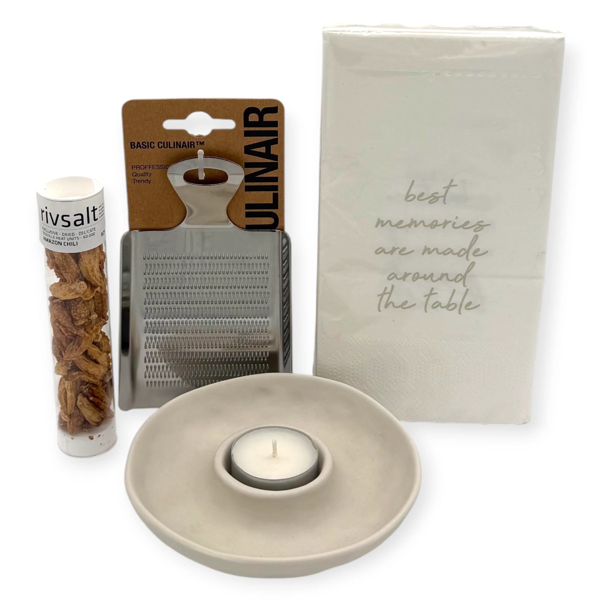 Close-up of the Candlelight Dinner Letterbox Gift contents: Rivsalt Amazon Chili tube, stainless-steel grater, ceramic tealight holder with candle, and napkins reading “best memories are made around the table.”
