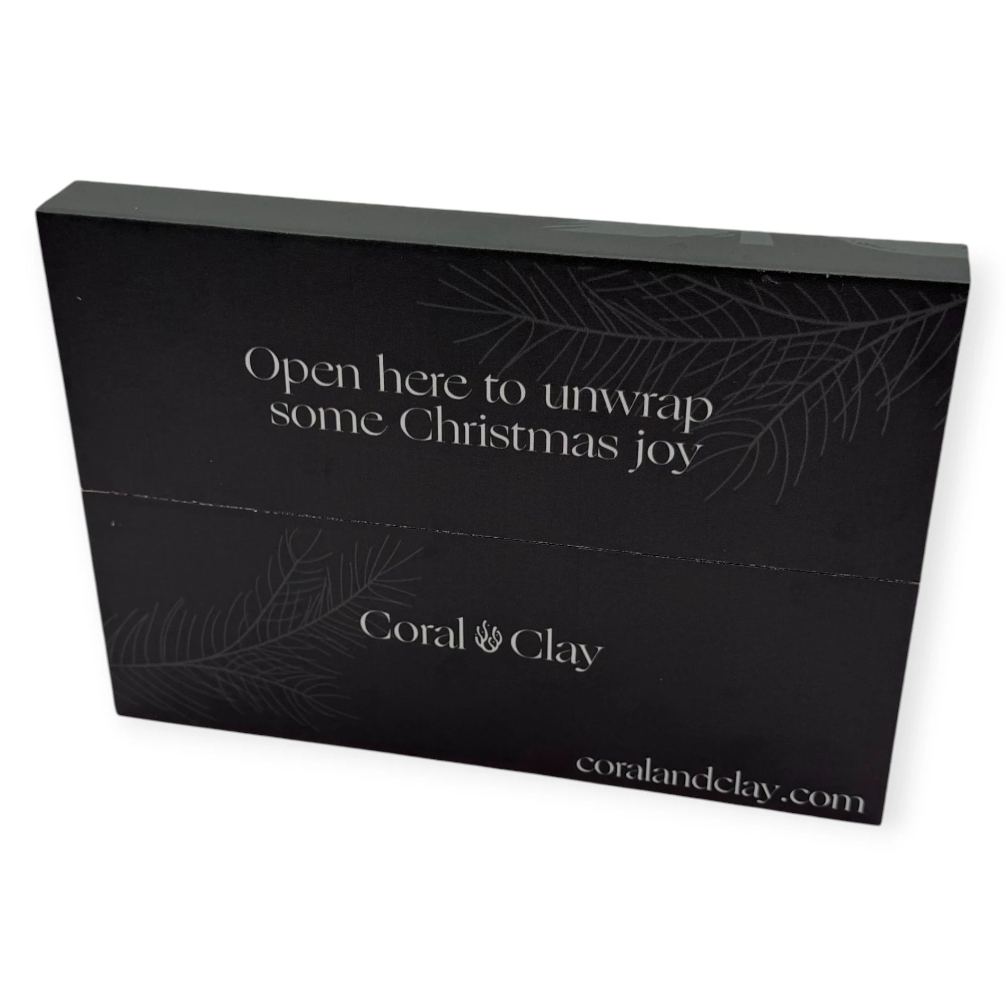 Back view of Coral & Clay deep forest green Christmas letterbox packaging with the message “Open here to unwrap some Christmas joy” and festive pine illustrations.