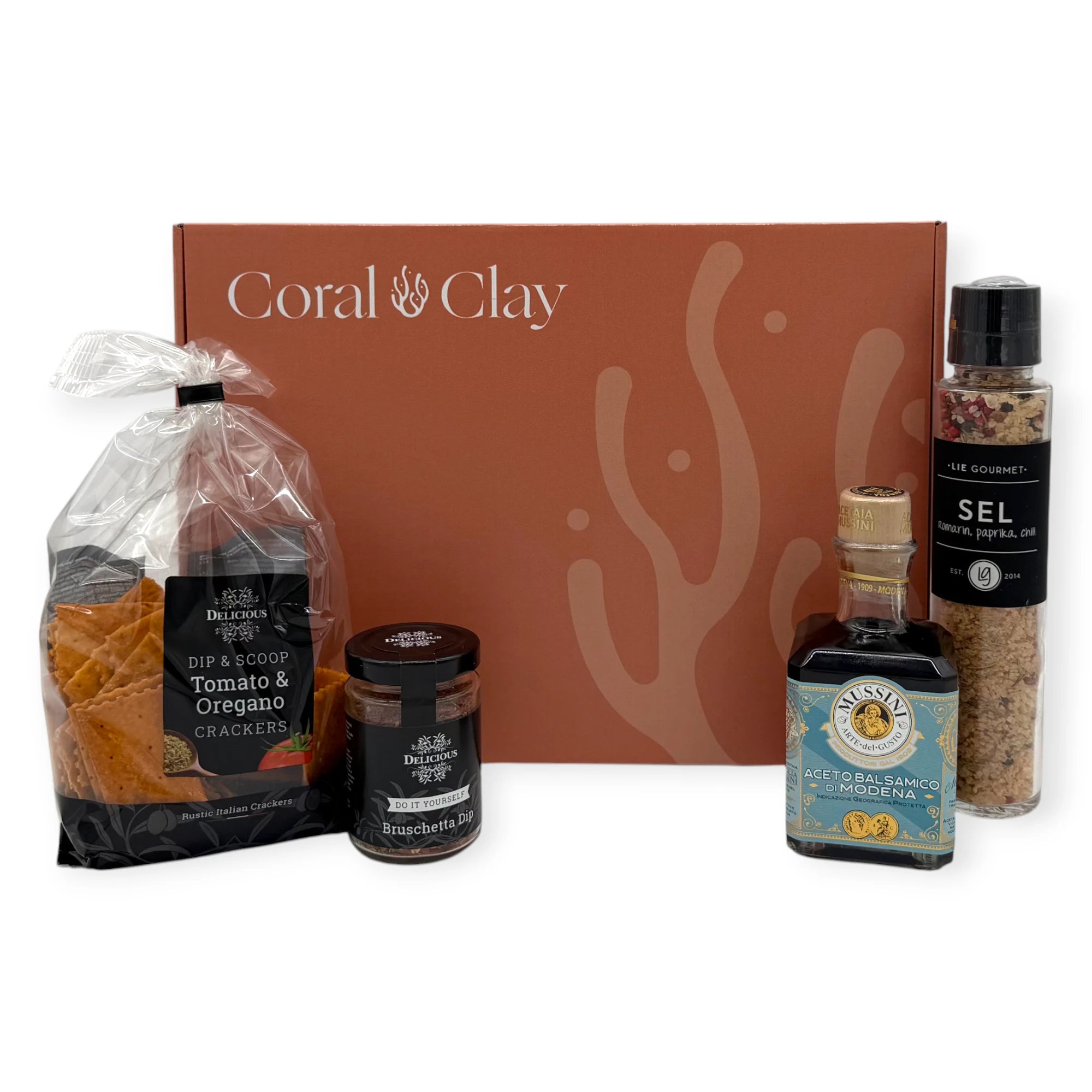 Gourmet cooking ingredients arranged in front of a Coral & Clay Signature Gift Box, featuring Lie Gourmet flavored salt, Mussini balsamic vinegar, Benolive rosemary olive oil, and two Delicious dip mixes.