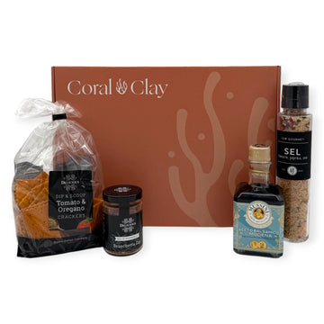 Gourmet cooking ingredients arranged in front of a Coral & Clay Signature Gift Box, featuring Lie Gourmet flavored salt, Mussini balsamic vinegar, Benolive rosemary olive oil, and two Delicious dip mixes.