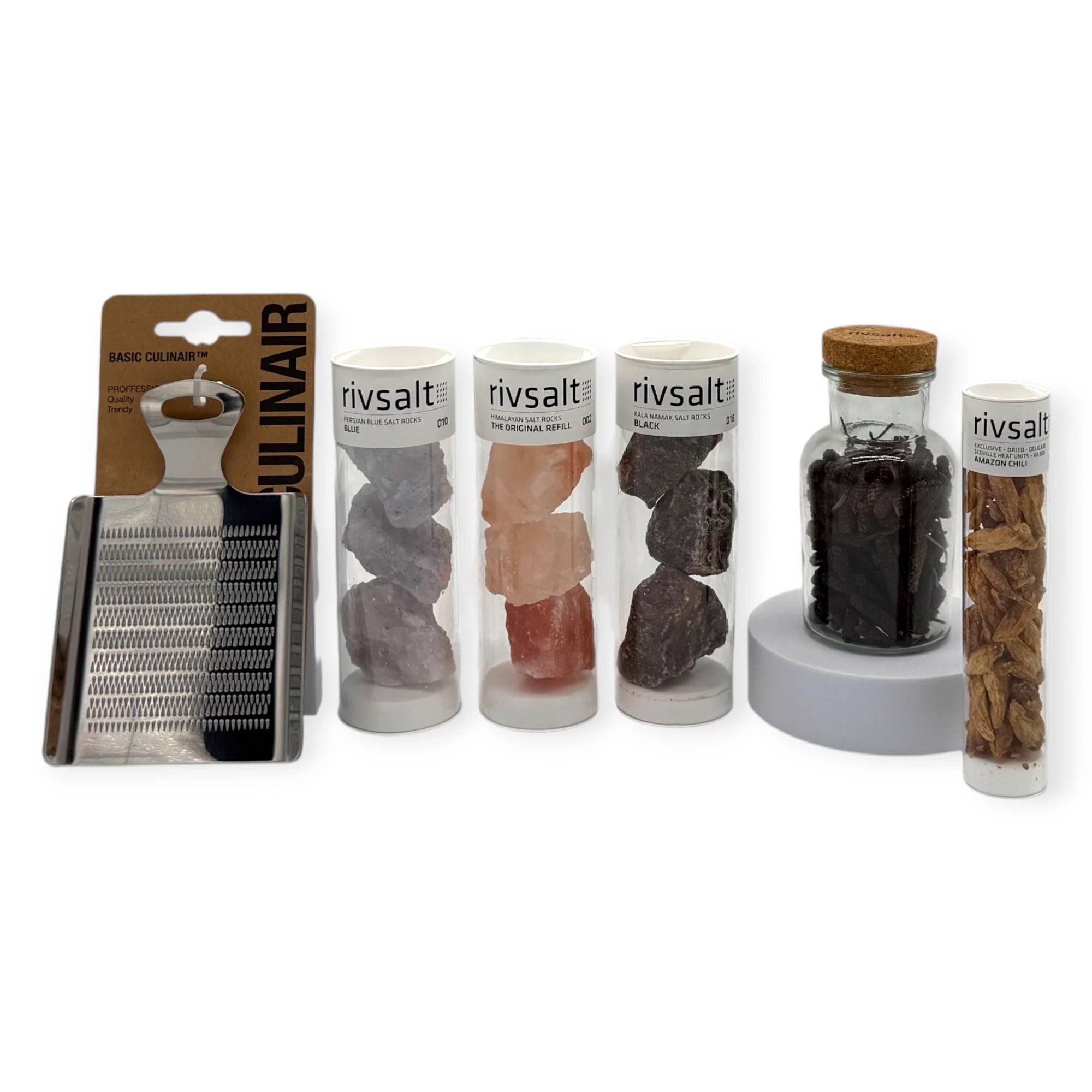 Rivsalt gourmet salt rock collection with grater set — including Persian blue salt rocks, Himalayan pink salt rocks, black Kala Namak salt rocks, Amazon chili refill tube, and a stainless-steel grater alongside a glass jar of whole spices.