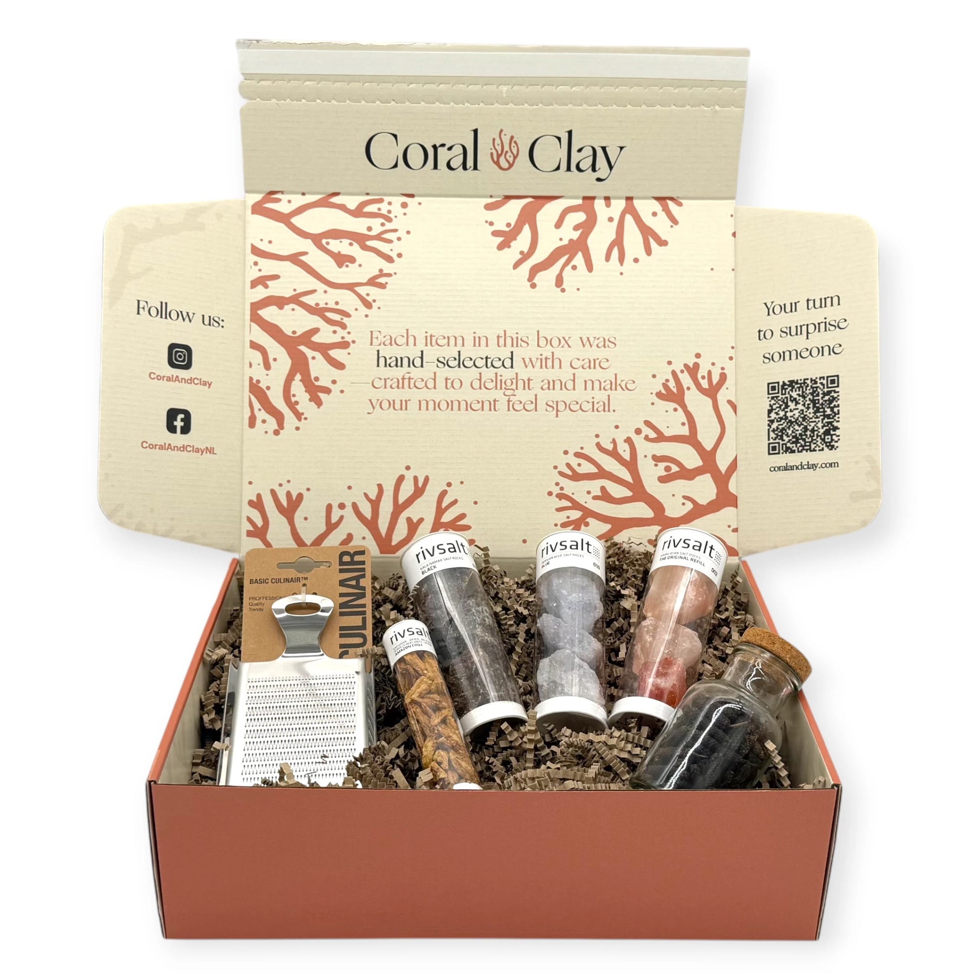 Open Coral & Clay gift box filled with Rivsalt salt rocks, Amazon chili tube, whole spice jar, and stainless-steel grater nestled in brown shredded filling.”