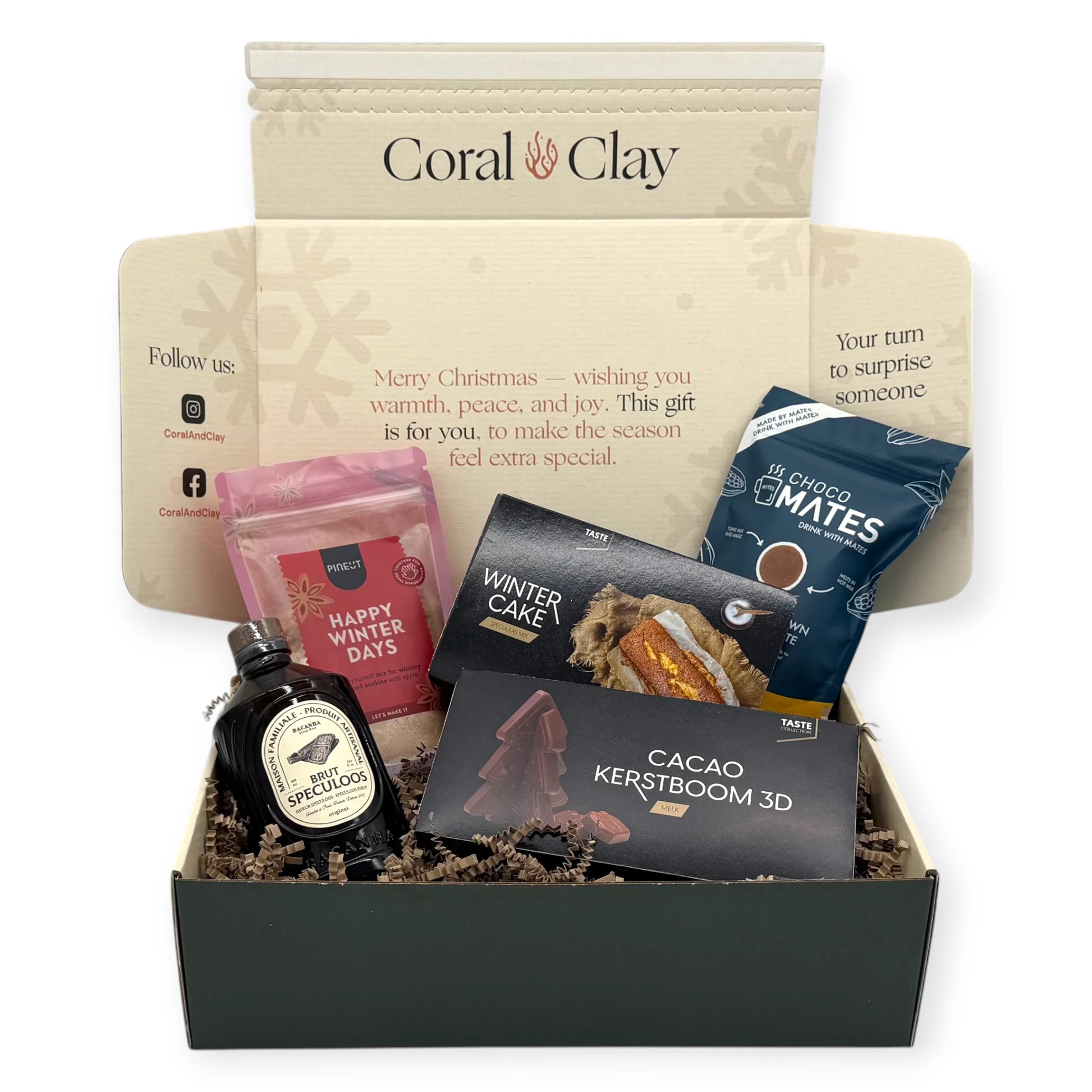 Top-down view of the Coral & Clay Winter Sweets Signature Gift Box opened to reveal Happy Winter Days cookie mix, Choco Mates hot chocolate balls, Winter Cake mix, 3D chocolate Christmas tree, and Speculoos liqueur nestled in kraft paper filling.